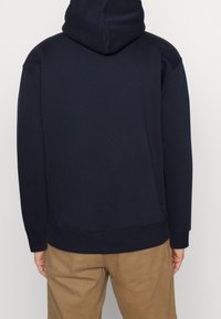 Sudadera azul marino hecha de una tela suave, con capucha ajustable, mangas largas y un corte holgado. Detalles de costura cerca del dobladillo.