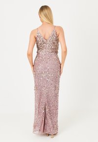 Largo vestido ajustado en suave rosa con intrincados adornos florales y lentejuelas, con tirantes ajustables y una abertura en la parte posterior.