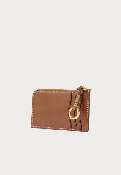 Carteira de couro castanho com textura suave, fecho de correr e detalhe em anel dourado. Apresenta costura decorativa e formato retangular compacto.