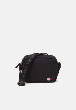 Kompaktowa czarna prostokątna torba na ramię z regulowanym paskiem, na którym znajduje się napis "Tommy Jeans" oraz mała naszywka z logo Tommy Jeans z przodu.