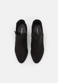 Svarta mockaskinn ankelskor med spetsig tå, sidoutskärningar och en slät, matt yta. Interiören visar varumärket "even&odd."