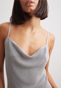 Camisole metallica argento con scollo a V e spalline sottili, realizzata in un tessuto morbido e testurizzato, con un design aderente.