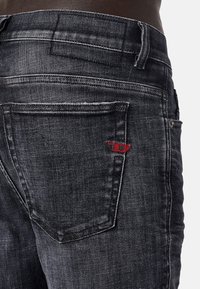 Mörkgrå denimjeans med en bakficka som har röd sömnadsdetalj. Materialet ser ut att vara urtvättat med en något strukturerad yta.