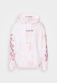 Růžová mikina s tie-dye vzorem, s kapsou na přední straně, kapucí se šňůrkou a vyšitým květinovým designem podél rukávů; obsahuje černý text.