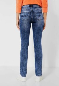 Blå denimjeans med rak bendesign, med en blekt textur, bakfickor och midjehöjd i normal nivå, kombinerat med vita sneakers.