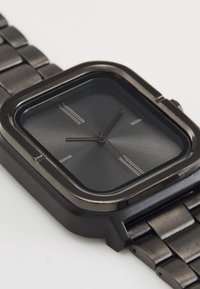 Montre bracelet en métal noir avec un boîtier carré, un cadran sombre et des index heures en argent. Équipée d'un bracelet en métal maillons pour un port sécurisé.