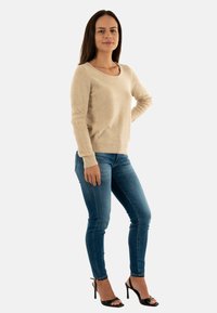 Maglione beige in morbido tessuto a maglia con scollatura rotonda e maniche lunghe. Abbinato a jeans blu aderenti e sandali neri con tacco alto.