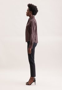 Camicia a maniche lunghe con bottoni in stampa scura con piccoli motivi floreali, abbinata a jeans neri aderenti e sandali neri con tacco alto.