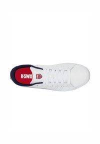 Weißer Sneaker mit einem strukturierten Leder-Obermaterial, marineblauen Akzenten, roter Innensohle und weißen Schnürsenkeln. Logo auf der Zunge angebracht. Klassisches Sportdesign.
