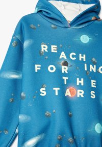 Sudadera con capucha en azul, con un estampado de galaxia que incluye planetas y rocas. Texto "ALCANZA LAS ESTRELLAS" en blanco. Tela suave, corte relajado.