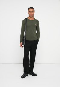 Cămașă verde cu mânecă lungă, cu un logo mic, asortată cu pantaloni negri și pantofi negri. Design simplu, textură netedă, siluetă ajustată.