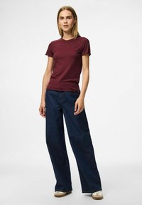 Burgunderfärgad ribbad kortärmad topp med vågig nederkant, tillsammans med vida mörk denimjeans. Enkel design med en texturerad finish.