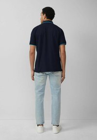 Navy polo shirt with turquoise accents, paired with light blue jeans and white sneakers. The fabric appears smooth and casual.