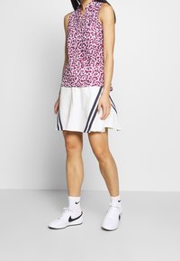 Oblíbený bezrukávový top s fialovo-bílým abstraktním vzorem, spojený s bílou rozšířenou sukní se navy pruhy a bílými teniskami.