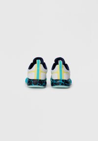 Des chaussures de sport avec un dessus blanc agrémenté de accents bleu et jaune, une semelle noire texturée avec des détails turquoise, et un onglet arrière bleu.