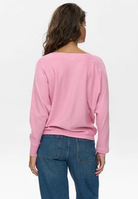 Top de manga larga rosa con un escote amplio y hombros caídos, combinado con unos jeans azules de tiro alto. La tela parece suave y ligeramente texturada.