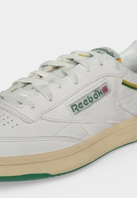 Λευκό δερμάτινο αθλητικό παπούτσι Reebok με μπεζ σόλα, πράσινη επένδυση και λογότυπο Union Jack στη πλευρά κοντά στα κορδόνια.