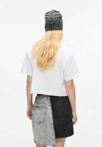 Trumpas baltas marškinėliai su trumpomis rankovėmis, derinami su dviejų spalvų džinsine sijoną – šviesiai pilka ir juoda. Pilka megzta kepurė ant galvos.