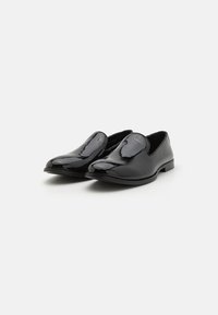 Melnas lakotas ādas loafers ar spīdīgu apdari, apaļu purngalu un bez auklām. Zema profila papēdis un gluda, eleganta forma.