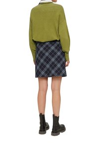 Grüner Pullover mit lässigem Schnitt, kombiniert mit einem marineblauen karierten Minirock mit hellblauen Akzenten und schwarzen Chelsea-Stiefeln.
