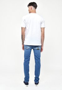 T-shirt bianco in cotone abbinato a jeans di denim azzurri chiari, con una sottile trama e tasche posteriori cucite. Le sneakers completano l'outfit.