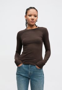 Καφέ μακρυμάνικη μπλούζα από απαλό ύφασμα με στρογγυλή λαιμόκοψη και εφαρμοστή γραμμή, συνδυασμένη με μπλε τζιν παντελόνι που έχει ελαφριές διακοσμητικές λεπτομέρειες.