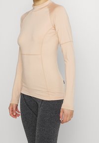 Ljust beige långärmad träningstop med hög krage och åtsittande design. Slät tyg med sömmar längs kroppen för en strukturerad look.