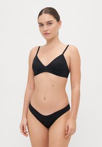 Črni bikini komplet, ki vsebuje trikotno bivšo odprtino z tankimi naramnicami in ujemajoče se nizko visokimi hlačkami. Gladek material brez vidnih vzorcev ali kovinskih delov.