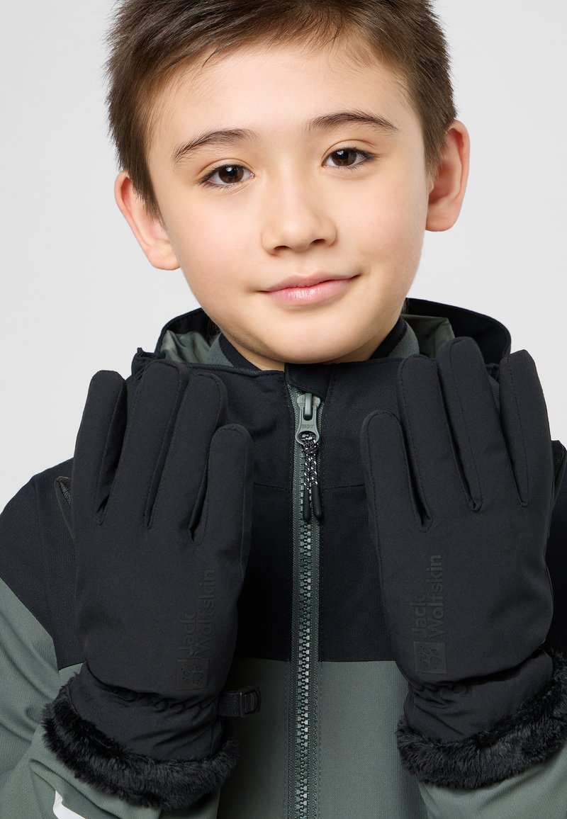 Schwarze Handschuhe mit einer strukturierten Oberfläche und Kunstfellbündchen, die ein Logo am Handgelenk aufweisen. Getragen von einem Kind in einer zipfeljacke.