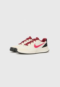 Nike sneakers med en cremefarvet overdel, røde snørebånd og logo, sort hælkappe, struktureret ydersål og et rundt tådesign.