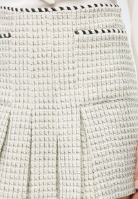 Witte tweed rok met zwarte accenten, met een gestructureerd geweven patroon, twee zakken en plooien aan de onderkant.