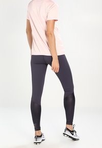 Leggings grises con una tela suave y elástica, con detalles oscuros y recortes en la parte inferior de las piernas, combinados con una camiseta rosa claro.