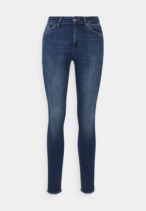 Jeans justos feitos de denim azul escuro. Inclui fechamento frontal com botão e ziper, design de cinco bolsos e barras de tornozelo desfiadas.