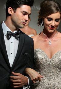 Bräutigam in einem schwarzen Smoking mit einer karierten Fliege, Braut in einem mit Perlen verzierten, elfenbeinfarbenen Kleid mit Herz-Ausschnitt und filigranen Verzierungen.