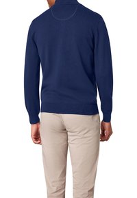 Pull bleu marine avec un col haut, des manches longues, et des poignets et ourlet côtelés. Texture en maille lisse, porté avec un pantalon de couleur claire.