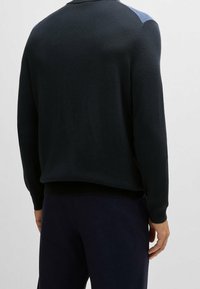 Mörk marinblå tröja med långa ärmar, ribbade muddar och nederkant. Har ljusblå detaljer på axlarna. Slät stickad yta.