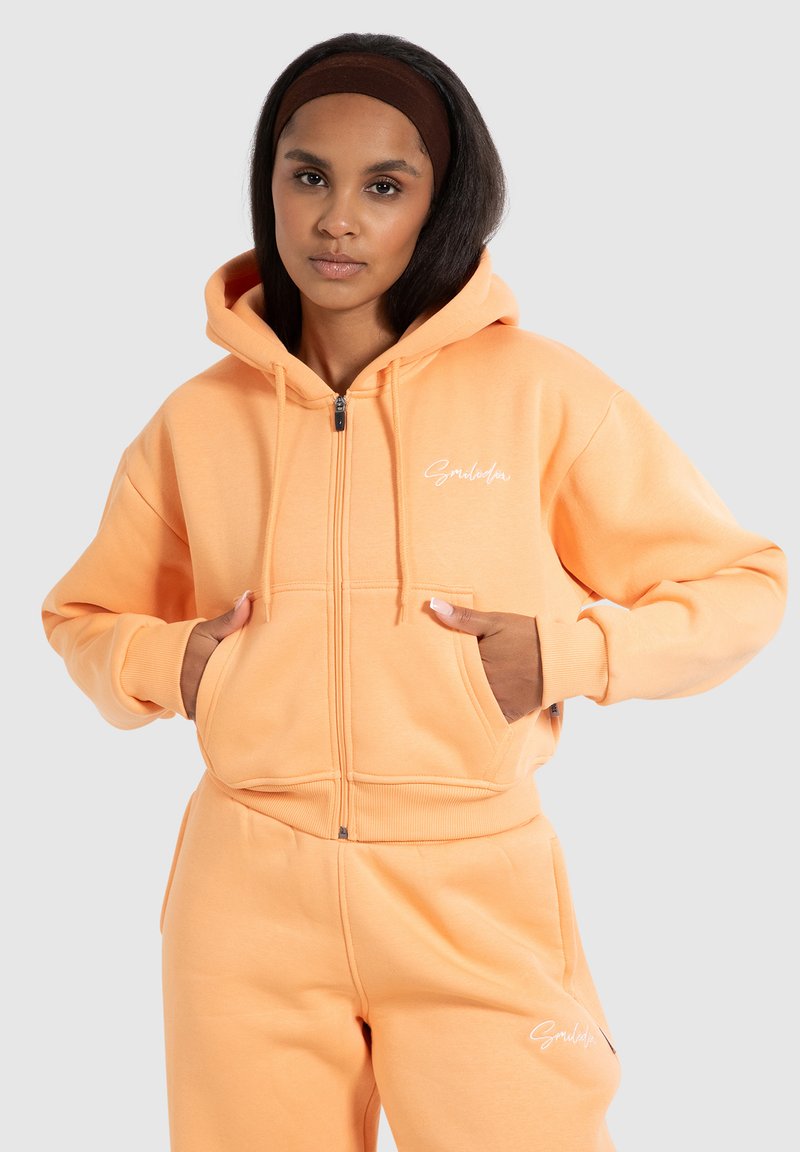 Persika zip-up hoodie i mjuk bomullsblandning, med en frontficka i kängurustil, dragsnören och ribbade ärmslut. "Smilodon"-logotyp på bröstet.