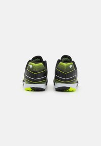 Zapatillas deportivas negras con un acabado texturizado, que presentan detalles en verde, franjas reflectantes y una suela blanca con un agarre amarillo brillante.