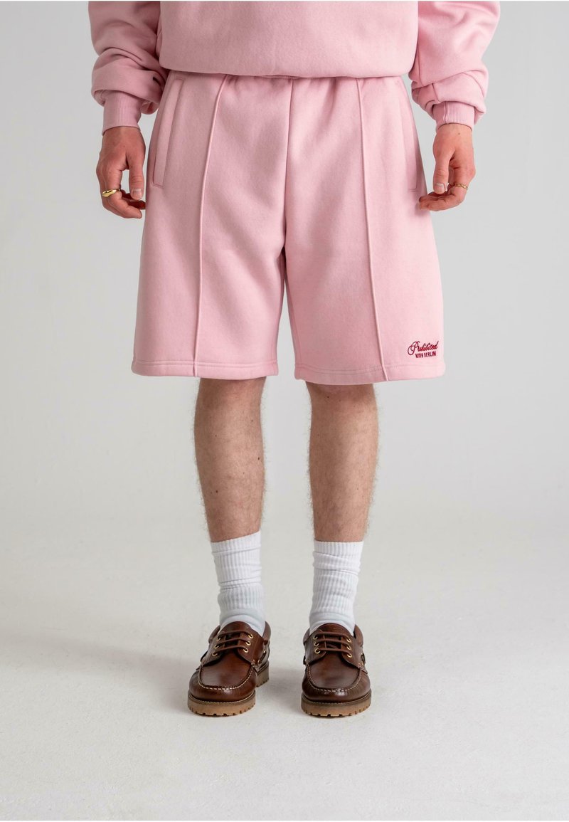 I pantaloni corti in pile rosa presentano una vestibilità morbida, due tasche laterali e dettagli cuciti. Abbinati a scarpe marroni e calze bianche.