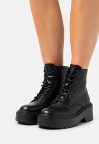 Černé kožené kotníkové boty s kulatou špičkou, šněrováním v přední části a masivní platformou. Hladký povrch s robustními švy.