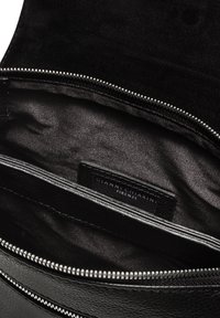 Interno di una borsa di pelle nera con una superficie liscia, dotata di chiusura a zip e una piccola etichetta. L'imbottitura è in un tessuto lucido di colore nero.