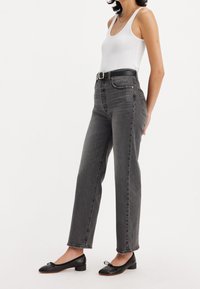 Jeans de mezclilla gris de cintura alta con un corte recto, que presentan detalles de costura sutiles y un cinturón negro, combinados con zapatos planos negros.