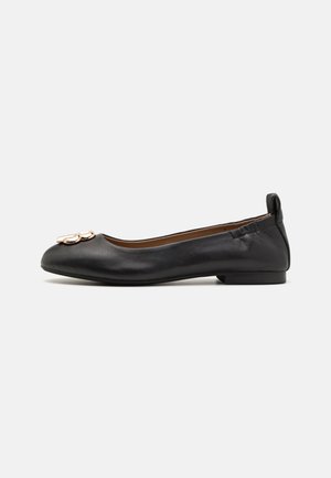 Ballerine plate en cuir noir avec un bout arrondi, un talon fin et un ornement métallique décoratif sur le bout. Texture lisse avec un design ajusté.