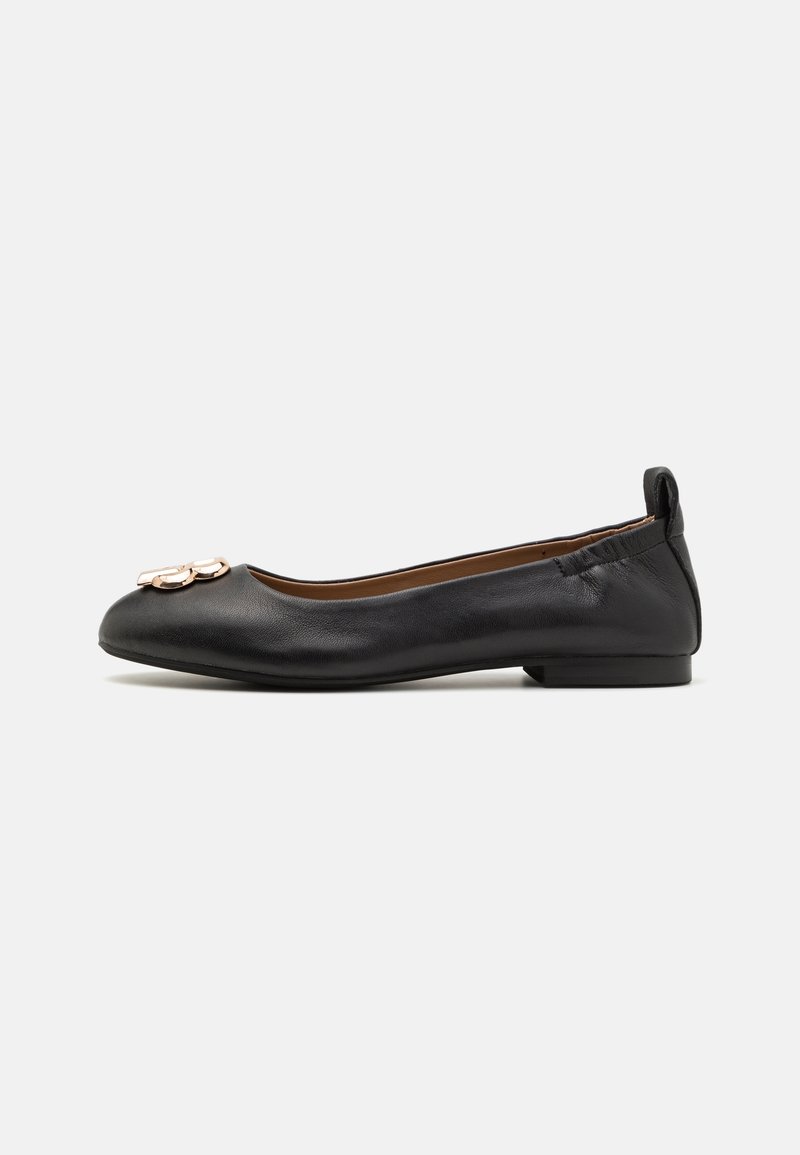 Ballerine plate en cuir noir avec un bout arrondi, un talon fin et un ornement métallique décoratif sur le bout. Texture lisse avec un design ajusté.