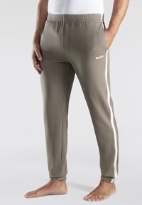 Grijze sportbroeken met een elastische tailleband, zijzakken, witte strepen langs de benen en een klein logo op de dij.