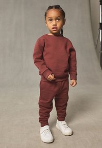 Ensemble sweat-shirt et pantalon de jogging bordeaux en coton doux, avec poignets côtelés et petit logo. Associé à des baskets blanches.