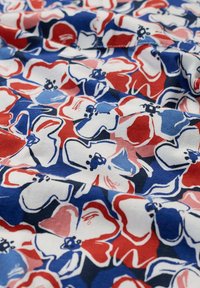Tela de algodón con un patrón floral en tonos rojos, azules y blancos. El diseño presenta flores superpuestas con detalles contorneados y una superficie texturizada.