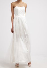 Abito bianco senza spalline con corpino in pizzo e una gonna leggera e fluente in chiffon. Presenta una vita aderente e un morbido strato in tulle.