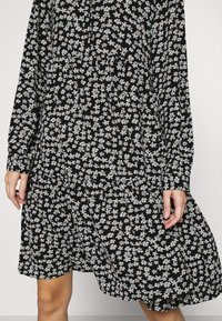 Abito nero con maniche lunghe, motivo floreale in blu chiaro e bianco, vita arricciata e vestibilità rilassata. Tessuto morbido con una silhouette fluida.