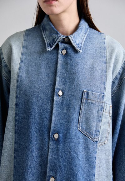 Denim krekls ar apkakli, pogu priekšpusi un krūšu kabatu; izgatavots no dažādiem zilā denim krāsu toņiem; redzami šuvju detalizējumi.